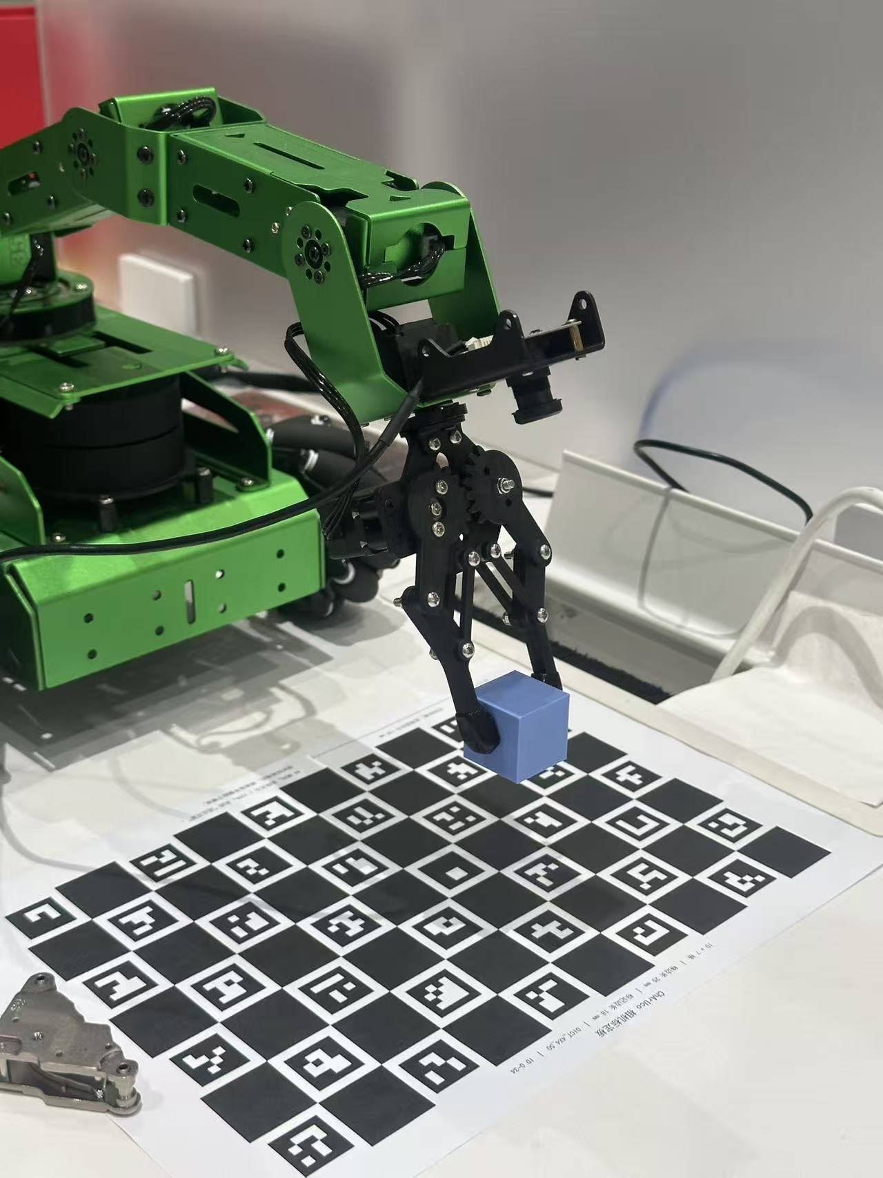 Green robotic arm gripping a blue cube above a calibration board